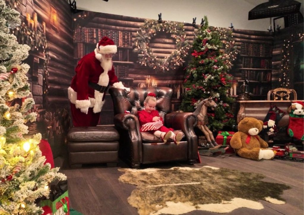 Santa watching little girl open her Christmas gift