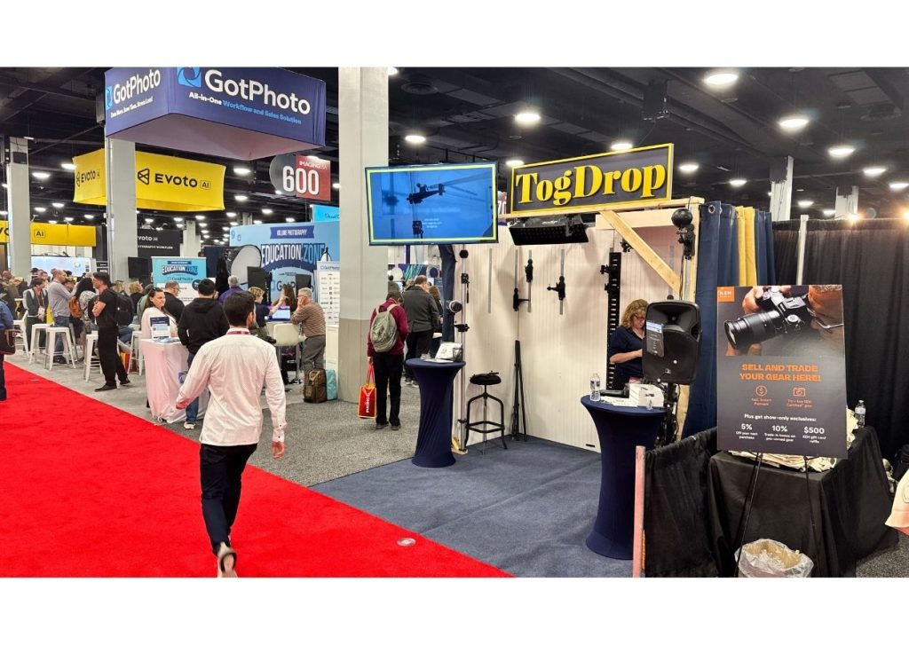 Photographers walking the trade show floor at a busy photography conference with vendor booths and live demos in the background