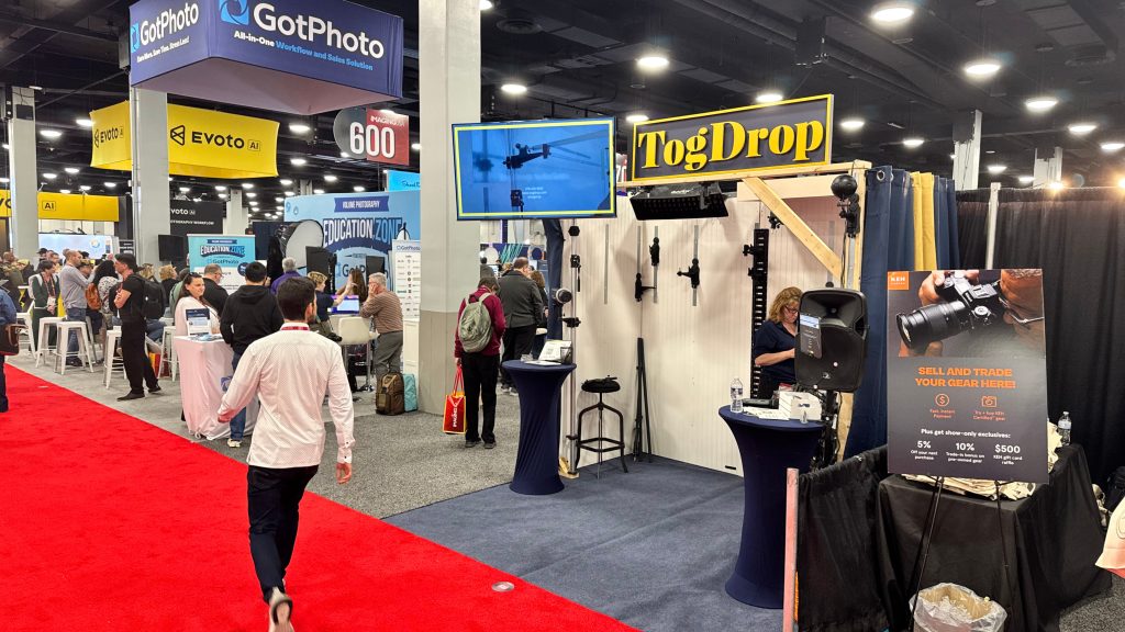 Photographers walking the trade show floor at a busy photography conference with vendor booths and live demos in the background