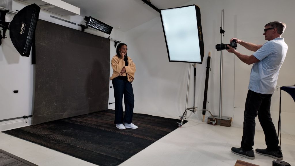 Photographer shooting portrait with simple backdrop setup in organized photography studio