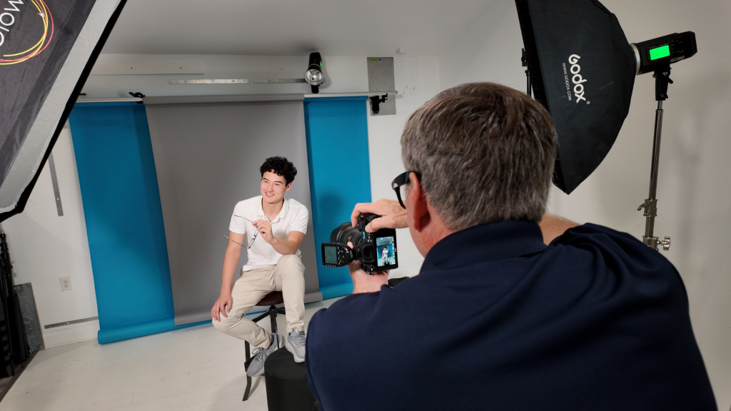 Photographer taking senior portraits in a small organized studio setup